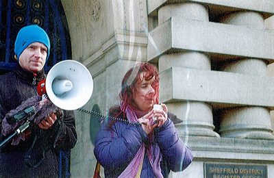 picture of dawn holding a microphone in front of Sheffield District Register Office, with a gentleman on the right holding the speaker for the microphone